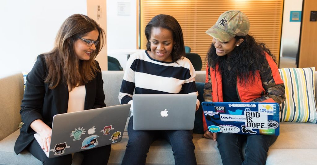 Three women working together on laptops in a casual office setting, emphasizing teamwork and collaboration.