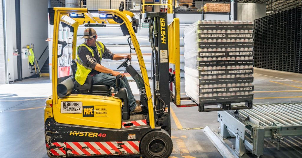 A warehouse worker maneuvers a forklift to transport crates for brewing company storage.