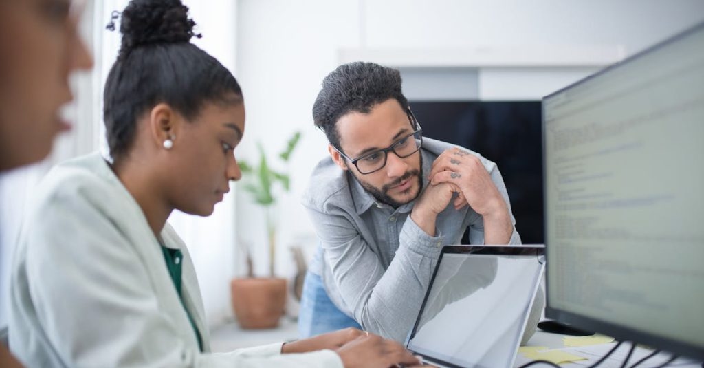 Two people collaborate in a modern office setting, focused on computer work